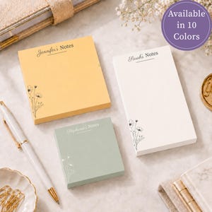 May include: Three rectangular paper notepads in yellow, white, and sage green. Each pad features a custom name at the top followed by the word Notes and a delicate black line drawing of wildflowers in the bottom corner. A white pen is included.