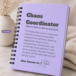 May include: A lavender spiral-bound notebook featuring the dark gray text Chaos Coordinator, a phonetic pronunciation, and a definition describing a person who manages tasks, plus the text Also known as: Katie in a script font at the bottom.
