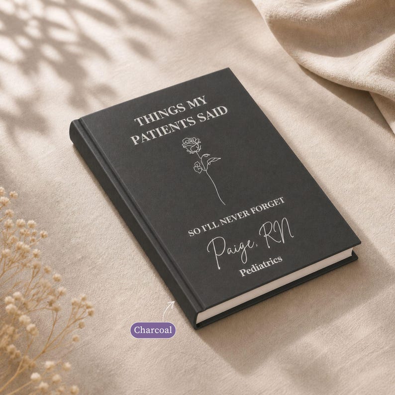 Charcoal “Things My Patients Said” nurse journal personalized hardcover notebook shown on a soft neutral fabric background with dried florals. This custom RN memory book features the name Paige, RN with Pediatrics, making it a thoughtful hospital gift, nurse appreciation gift, healthcare worker notebook, shift notes journal, patient quotes keepsake, and medical professional memory book.