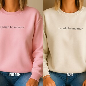 May include: Two sweatshirts, one light pink and one sand-colored, are displayed. Each has the phrase "i could be meaner" printed in a dark font across the chest. The light pink sweatshirt has "LIGHT PINK" printed below the neckline.