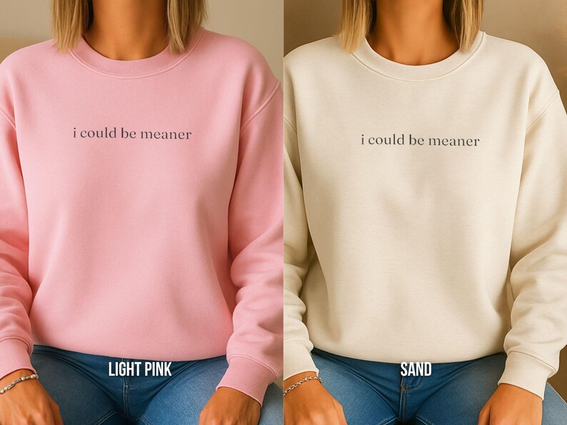 May include: Two sweatshirts, one light pink and one sand-colored, are displayed. Each has the phrase "i could be meaner" printed in a dark font across the chest. The light pink sweatshirt has "LIGHT PINK" printed below the neckline.