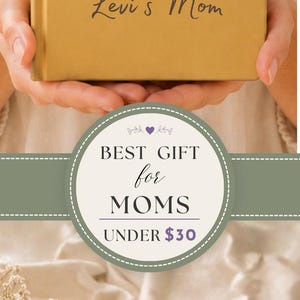May include: A mustard yellow hardback journal featuring the text Things My Child Says So I'll Never Forget, two white handprint illustrations, and the name Levi's Mom printed on the front cover. The journal is held upright against a neutral background.