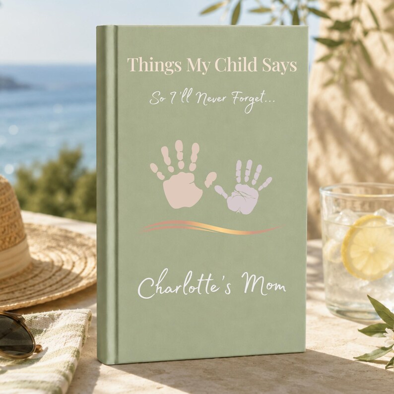 May include: A sage green hardback journal with the text Things My Child Says So I'll Never Forget... printed in white, featuring two light pink handprint illustrations, a gold wavy line, and the name Charlotte's Mom in white script font.