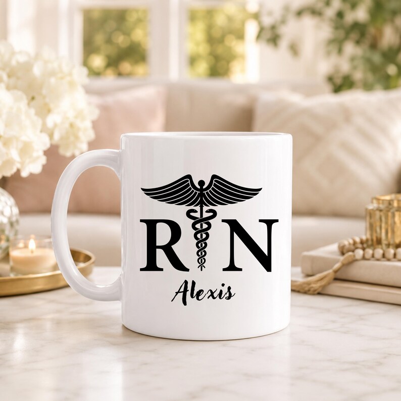 May include: A white ceramic mug featuring a black caduceus symbol centered between the letters R and N. Below the symbol, the name Alexis is printed in a black script font. The mug has a smooth finish and a curved handle on the left side.