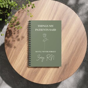 May include: A sage green spiral-bound notebook featuring the white text "THINGS MY PATIENTS SAID", "SO I'LL NEVER FORGET", and "Zoey, RN", along with a simple white line-art illustration of a single rose centred on the front cover.