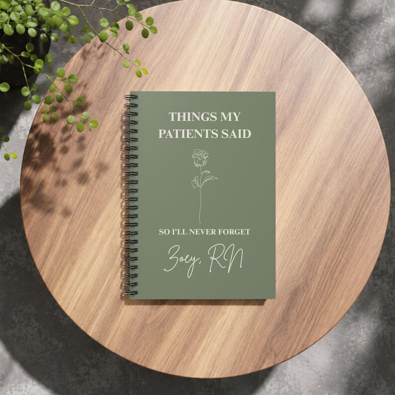 May include: A sage green spiral-bound notebook featuring the white text "THINGS MY PATIENTS SAID", "SO I'LL NEVER FORGET", and "Zoey, RN", along with a simple white line-art illustration of a single rose centred on the front cover.