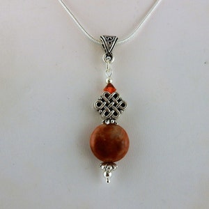 May include: A silver chain necklace with a silver Celtic knot pendant and a brown stone bead. The pendant has a small red crystal bead at the top.