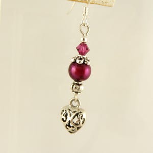 May include: Silver dangle earrings with a burgundy pearl, a silver heart charm, and a clear crystal bead.
