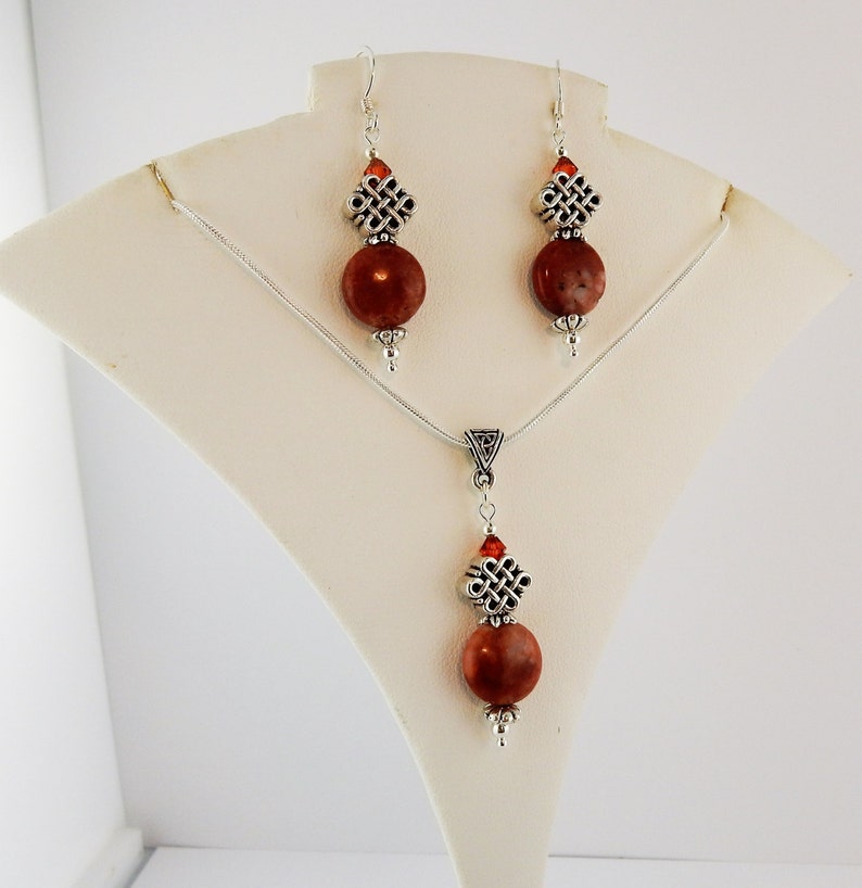 May include: A silver necklace and earrings set with brown stone beads and silver Celtic knot charms.