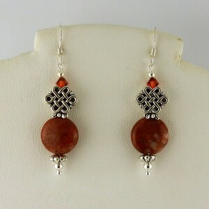 May include: A pair of silver earrings with a red stone and a silver Celtic knot design.
