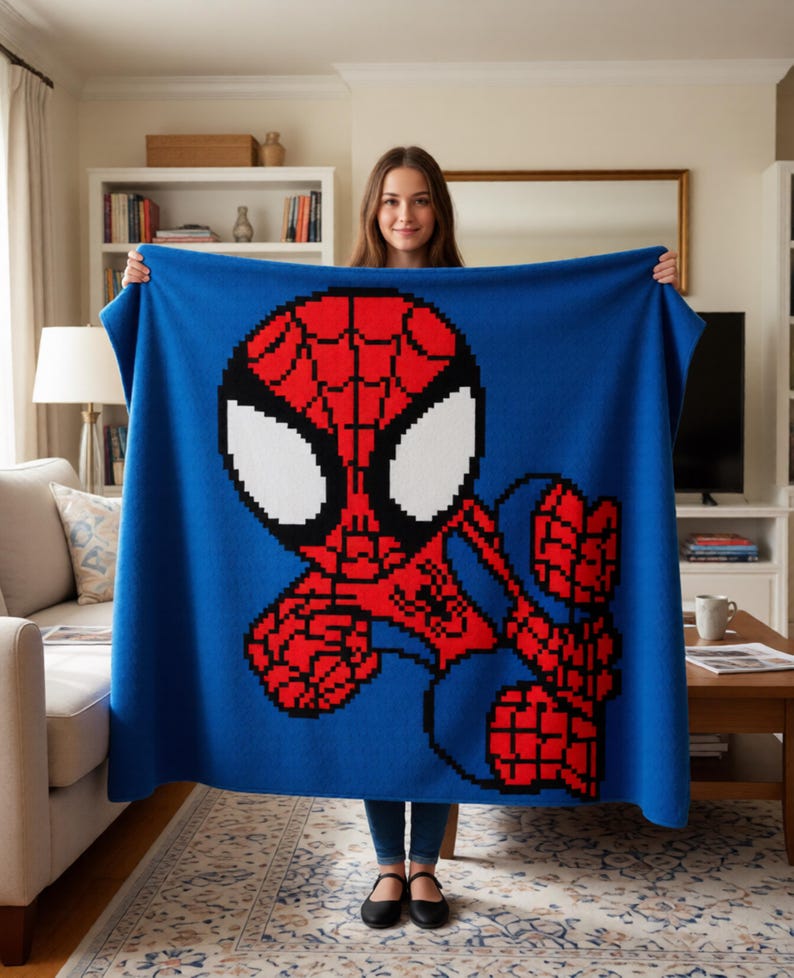 May include: A blue blanket with a pixelated Spider-Man design. The superhero is depicted in red, black, and white against a blue backdrop. The blanket is held up, displaying the full image of the character.