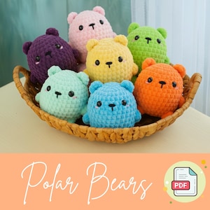 以下が含まれることがあります： 紫、ピンク、黄色、緑、青、オレンジなど、さまざまな色の編みぐるみのシロクマのぬいぐるみ7つが入ったバスケット。バスケットの下には「Polar Bears」という文字が筆記体で書かれています。
