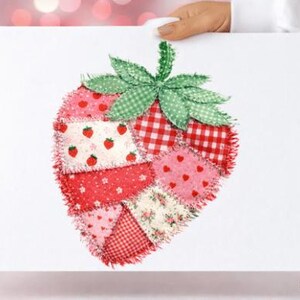Könnte beinhalten: Ein handgefertigtes Erdbeerdesign auf weißem Hintergrund. Die Erdbeere besteht aus verschiedenen rot- und rosafarbenen Stoffen mit Mustern, darunter Vichy und Tupfen. Grüne Stoffblätter zieren die Oberseite. Das Bild wird von einer Hand gehalten.