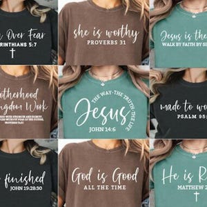 Può includere: Una collezione di nove magliette in vari colori, ognuna con una diversa citazione religiosa in scrittura bianca. Le magliette sono in tonalità di nero, marrone e verde acqua. Le citazioni includono "Faith Over Fear", "She is Worthy" e "Jesus is the Light".