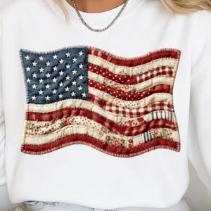 Könnte beinhalten: Weißes Sweatshirt mit einem verblassten Design der amerikanischen Flagge. Die Flagge hat einen Patchwork-Stil mit blauen Sternen, roten und weißen Streifen und floralen Mustern. Das Design befindet sich auf der Vorderseite des Sweatshirts.