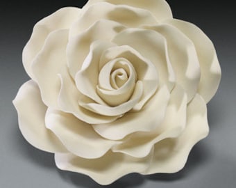 May include: A large, off-white rose sculpture with detailed petals. The flower is fully bloomed, showcasing the intricate layers and textures of the petals. The sculpture is likely made of ceramic or a similar material, and is set against a neutral background.