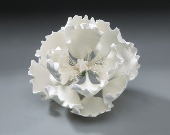 May include: A large, white, ceramic flower with ruffled petals. The flower has a detailed center with delicate stamens and pistils. The petals have a textured, wavy edge. The flower is a decorative item.