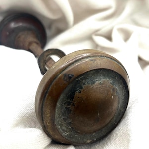 May include: Close-up of an antique brass door knob with a circular design. The knob has a dark, aged patina, showing signs of wear and use. The handle is attached with a small ring.
