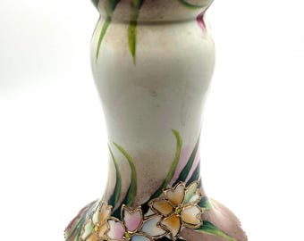 May include: A ceramic candlestick holder featuring a white base with a flared top and bottom. The surface is decorated with hand-painted pink and blue flowers, green leaves, and soft brown shading. The edges are finished with a thin gold trim.