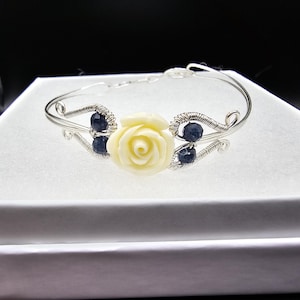 May include: A silver wire wrapped bracelet with a white rose charm and blue gemstone accents.