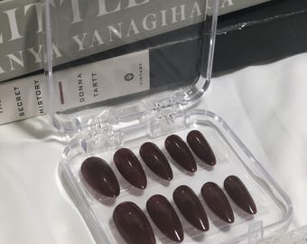 May include: A clear plastic case containing ten burgundy-coloured false nails. The nails are coffin-shaped and arranged in two rows of five.
