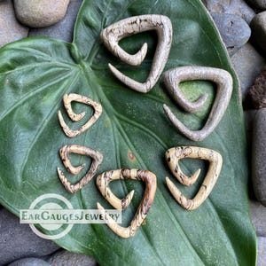 May include: A collection of wooden ear gauges in various sizes, featuring a unique triangular design with a natural wood grain pattern. The gauges are displayed on a large green leaf, with the text "Ear Gauges Jewelry" visible.