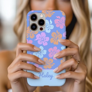 May include: A light blue phone case with a floral pattern of pink and orange hibiscus flowers. The case has a white stripe at the bottom with the name "Haley" written in cursive.