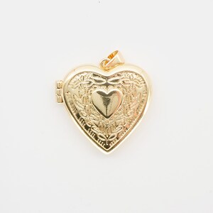 Op de afbeelding: Een goudkleurige hartvormige locket met ingewikkelde bloemen- en hartdetails. De locket heeft een kleine lus aan de bovenkant voor een ketting en een sluiting aan de zijkant. De locket is ongeveer 3,8 cm breed.