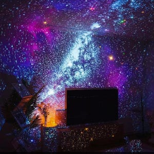 May include: A room ceiling and walls are illuminated with a vibrant star projection, creating a cosmic atmosphere. The display features a mix of blue, purple, and white light, simulating a starry night. The text at the bottom reads: High-Definition Full-Ceiling Star Projection.