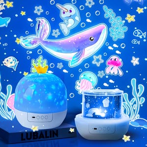 May include: A blue and white night light projector featuring a whale, narwhal, and jellyfish design. The projector displays a starry sky and ocean creatures. The word "LUBALIN" is printed on the base.