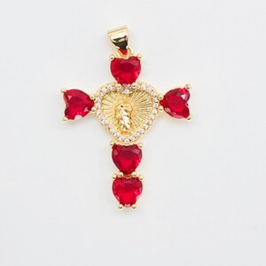 May include: Gold-tone cross pendant with red heart-shaped gemstones. The center features a gold heart with a religious figure and is surrounded by small clear stones. The pendant has a bail for a chain.