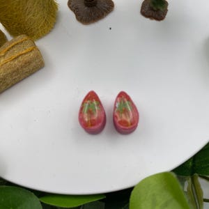 May include: Two small pink resin earrings with a green palm tree design.