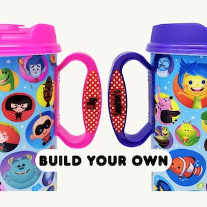 Puede incluir: Dos tazas de viaje de plástico con tapa, una con tapa y asa rosa, la otra con tapa y asa morada. Ambas tazas están decoradas con coloridas ilustraciones circulares de personajes. Las asas están personalizadas con los nombres Lily y Sophie's.