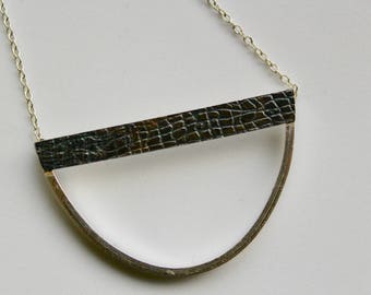 Puede incluir: Un collar de plata con un colgante de barra de cuero negro en forma de semicírculo.