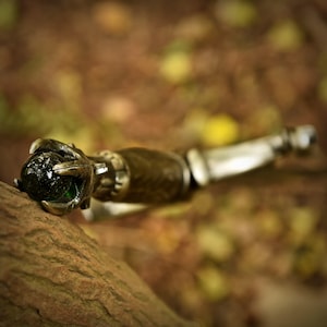 May include: A close-up of a decorative knife handle with a green gemstone set in a claw-like design. The handle is made of wood and metal.