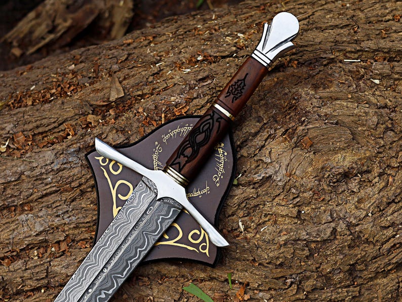May include: A detailed sword with a patterned blade and a wooden handle. The handle has intricate carvings and is set on a brown plaque with gold accents. The sword is displayed on a textured, brown surface.