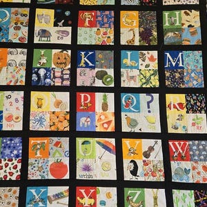 May include: A colorful patchwork quilt featuring the alphabet, with each letter displayed on a square. Each square has a letter and a corresponding image, such as an elephant for 'E' and a zebra for 'Z'. The quilt is on a black background.
