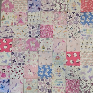 May include: A patchwork quilt composed of numerous square fabric patches featuring various prints including unicorns, rainbows, castles, ballerinas, fairies, stars, clouds, and Hello Kitty characters in shades of pink, purple, blue, and white.
