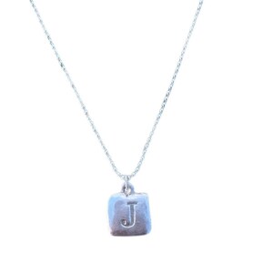 May include: A silver chain necklace with a square pendant featuring the letter J.