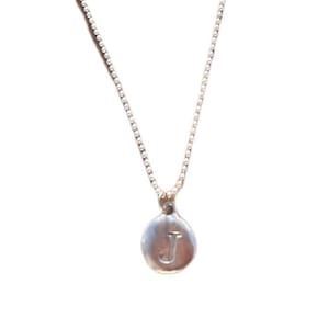 May include: A silver-colored necklace with a small, round pendant. The pendant features the letter "J" in the center. The necklace chain is delicate and hangs against a white background. The pendant is approximately 0.5 inches in diameter.