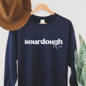 May include: Navy blue sweatshirt with the text "In my sourdough era" printed in white on the front.