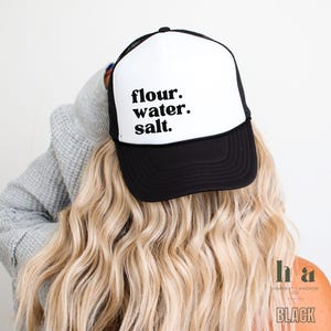 May include: A black and white trucker hat with the text "flour. water. salt." on the front. The hat is made by Harvest + Anchor Co. and is labeled "BLACK".