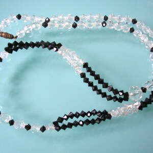 May include: A black and clear crystal necklace with a clasp. The necklace is made of faceted beads and is strung on a silver chain.