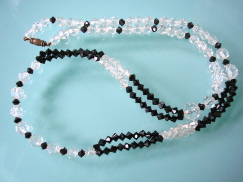 May include: A black and clear crystal necklace with a clasp. The necklace is made of faceted beads and is strung on a silver chain.