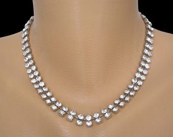 May include: A silver-toned necklace with multiple rows of clear, sparkling rhinestones. The necklace is displayed on a mannequin and has a classic, elegant design, perfect for formal occasions.