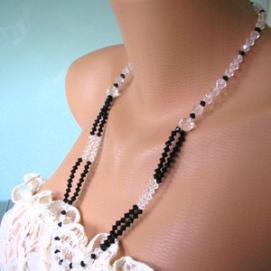 May include: A black and clear crystal beaded necklace. The necklace is on a mannequin wearing a white lace top.