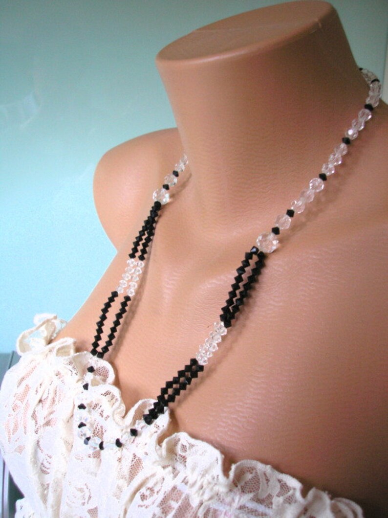 May include: A black and clear crystal beaded necklace. The necklace is on a mannequin wearing a white lace top.