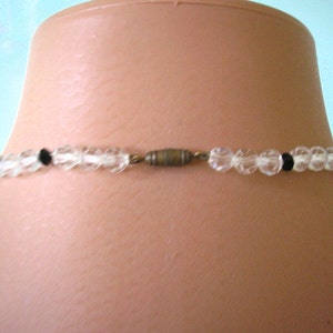 May include: A clear glass beaded necklace with black beads and a gold metal clasp.