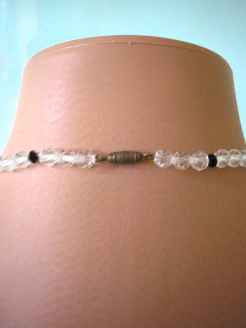 May include: A clear glass beaded necklace with black beads and a gold metal clasp.