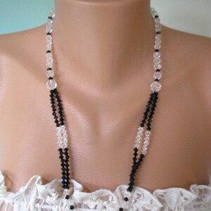 May include: A double strand necklace with alternating black and clear crystal beads. The necklace is displayed on a white lace-covered mannequin bust.